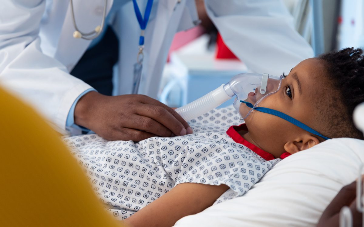 A doctor gently resting a hand on a child receiving oxygen in a hospital bed